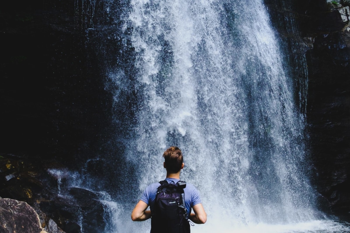 Man standing in front of a waterfall wearing a backpack