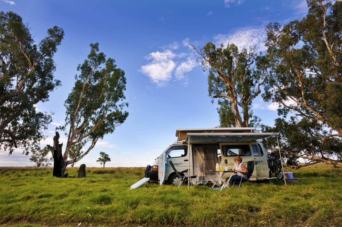 A woman sits at a table in front of her RV rental in a field