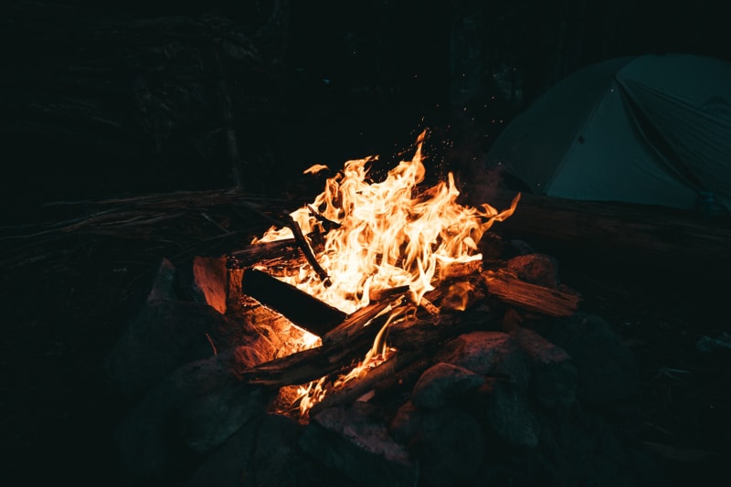 a dark photo of a campfire with a tent behind it