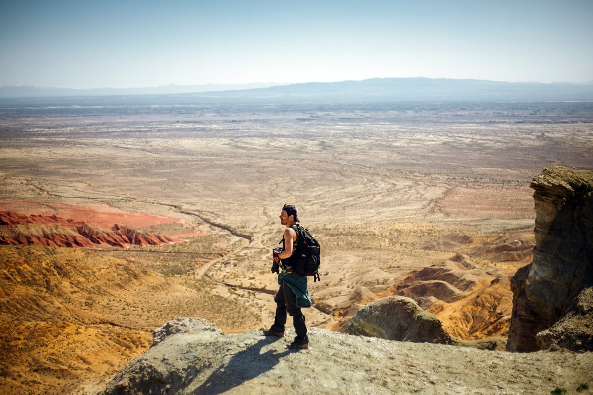 photographer with a backpack standing on a ledge overlooking a desert