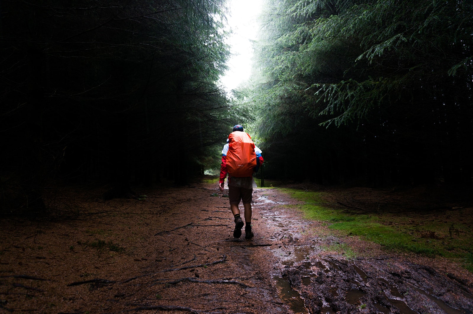a man with an orange backpack walking through a muddy trail