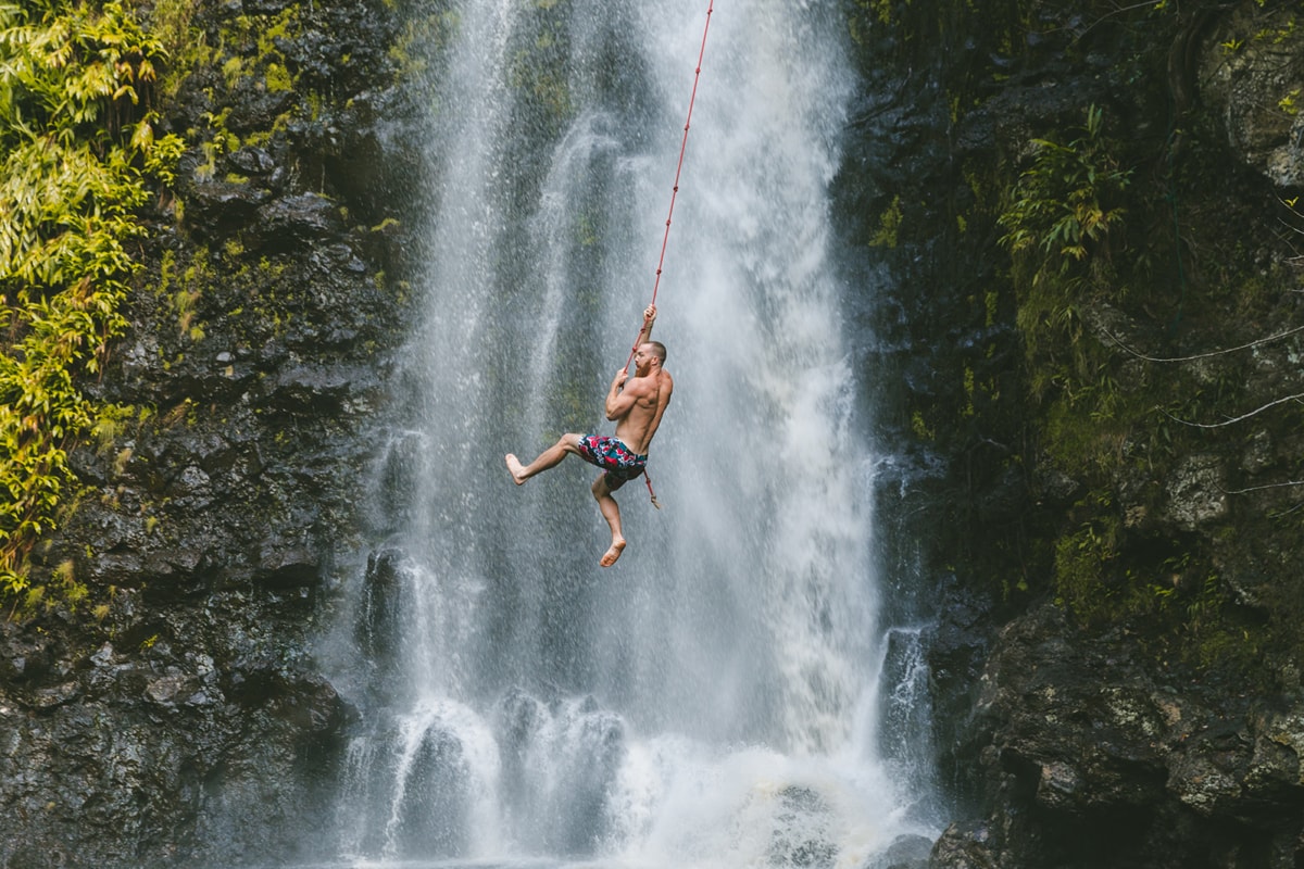 a man swings on a rope across a waterfall