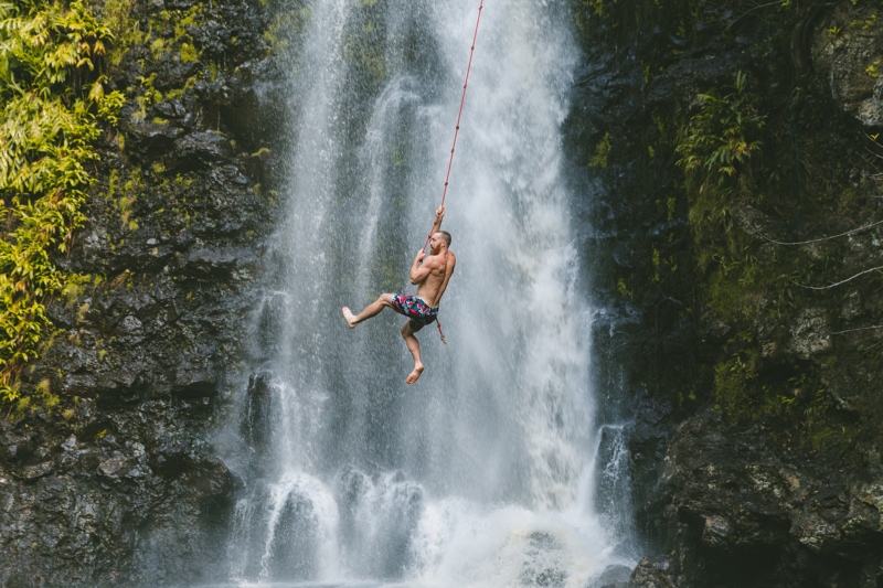 a man swings on a rope across a waterfall