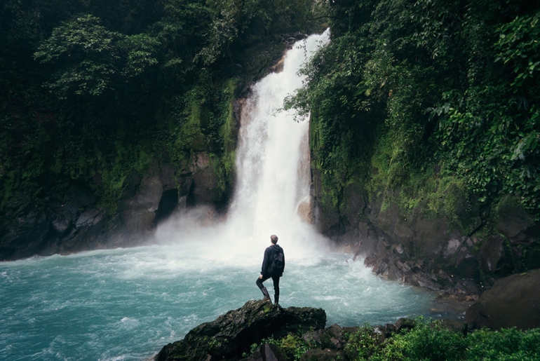 A man standing on a rock in front of a waterfall
