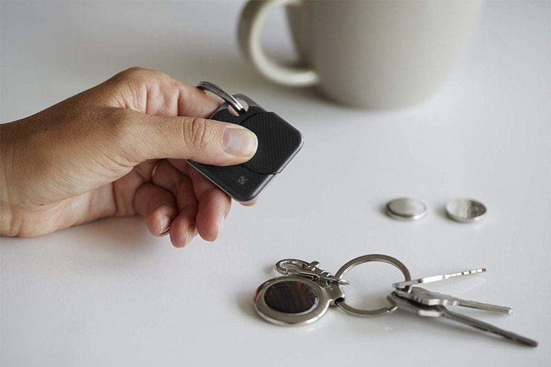 a hand holding a Tile Bluetooth Tracker next to a set of keys