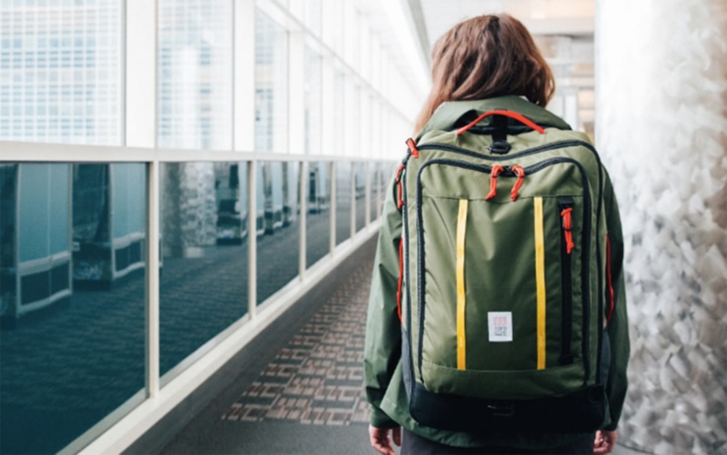 a woman walking through an airport with a Topo Designs Travel Bag