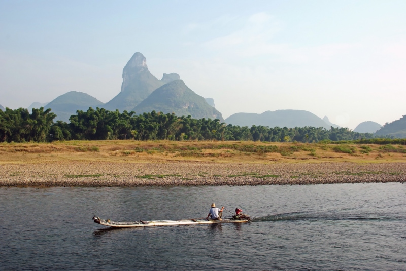 A man in a boat motors by the landscape in Yangshuo, China