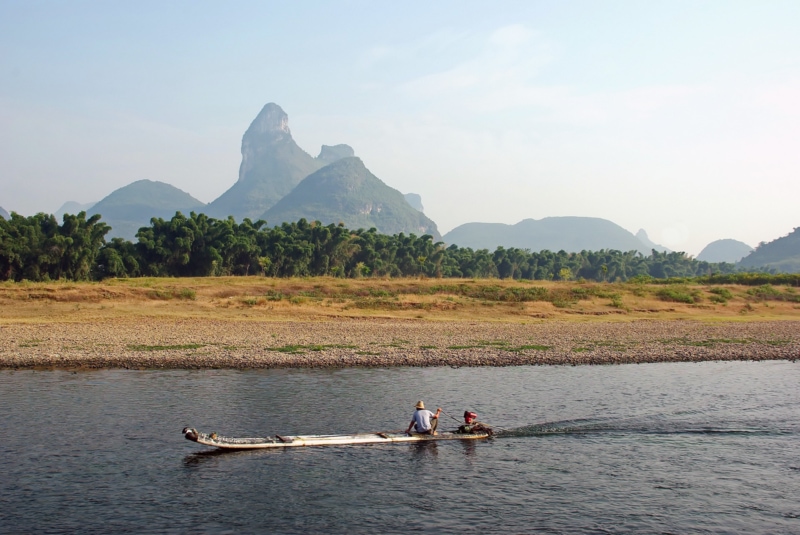 a man in a boat motors by the landscape in Yangshou, China