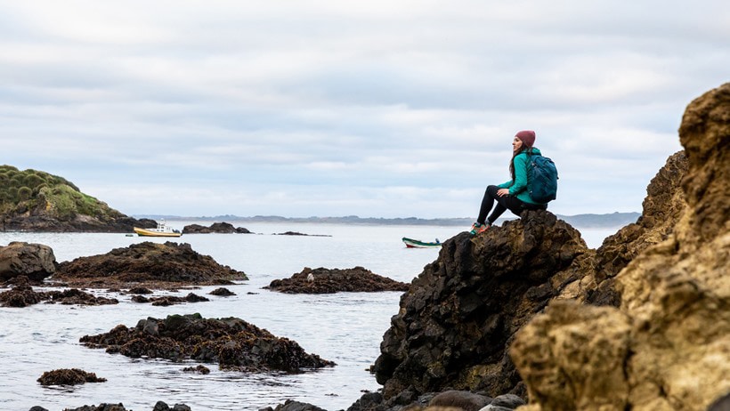 a woman sits on a coastal trail with an Osprey pack
