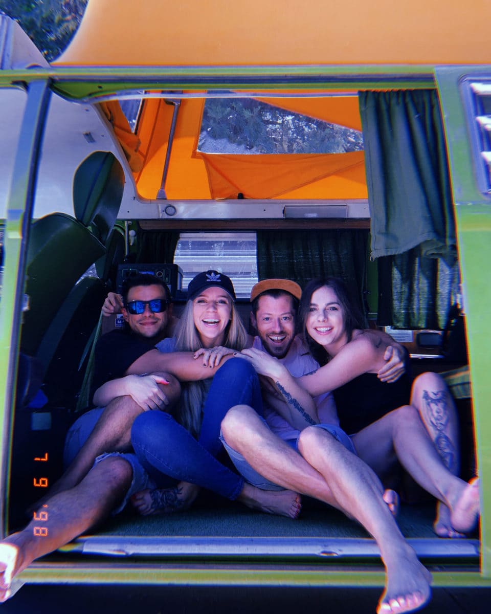 Four friends hanging out the back of a campervan rental