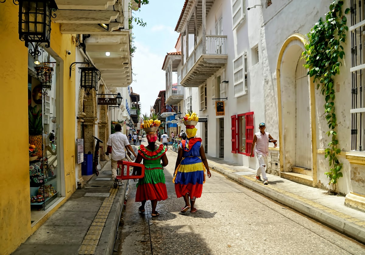 two women in colorful clothing walk down a street in Cartagena