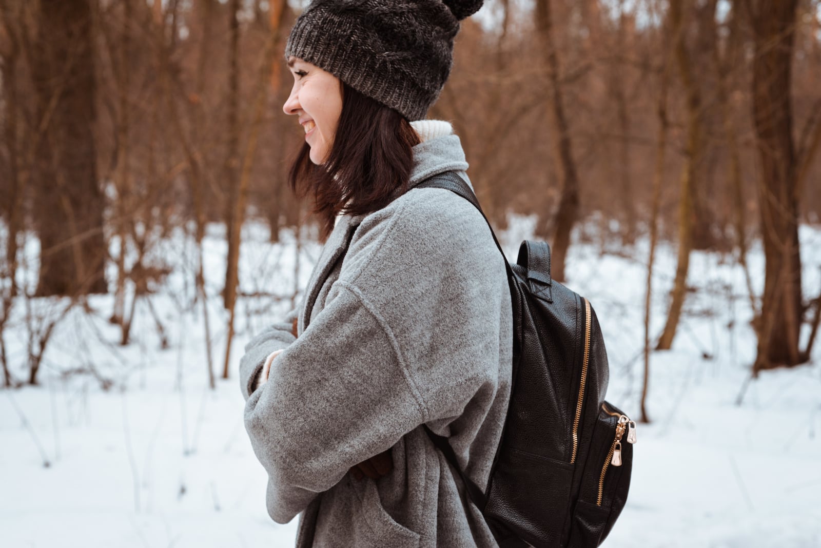 Portrait of a smiling girl with brown hair in winter forest wearing a leather backpack
