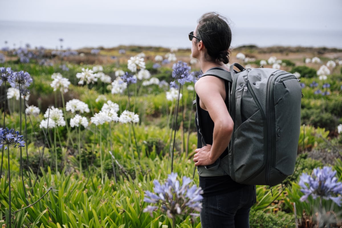 A woman standing in a field of flowers with her Peak Design Travel Backpack
