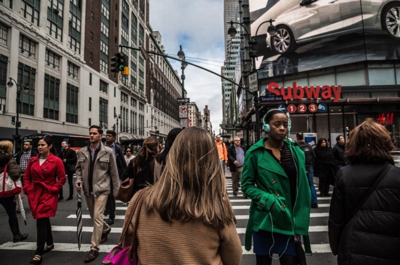 a young woman in a brown coat walks through a busy city intersection