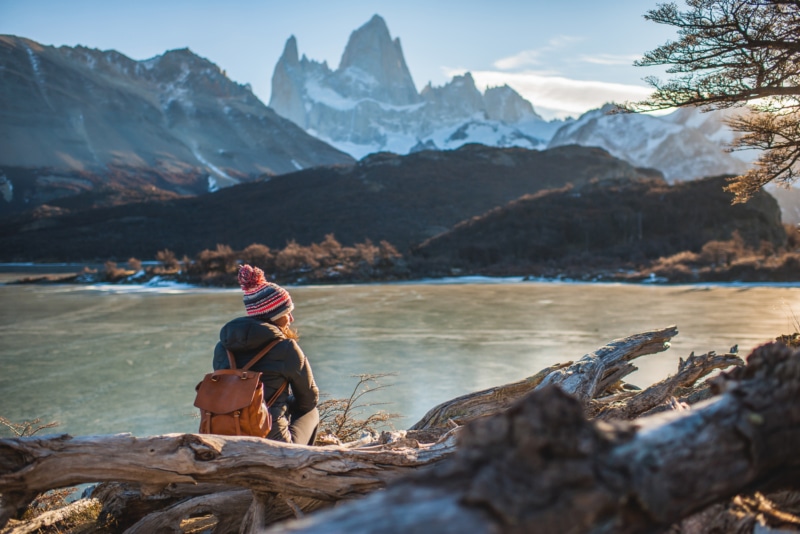 A woman with a leather backpack sits in front of Fitzroy Mountain in El Chalten, Argentina